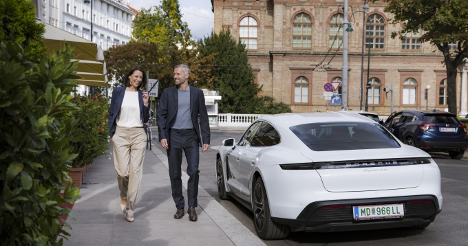 Žena i mu&scaron;karac &scaron;eću nogostupom i prolaze kraj bijelog Porschea